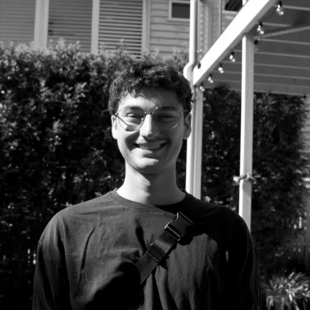 Black-and-white portrait of Sebastian Wells Chavez smiling outdoors, wearing glasses and a dark top